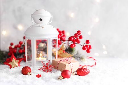 White lantern with candle, red decorations and berries on snow, horizontal Christmas or New year card with copyspaceの写真素材