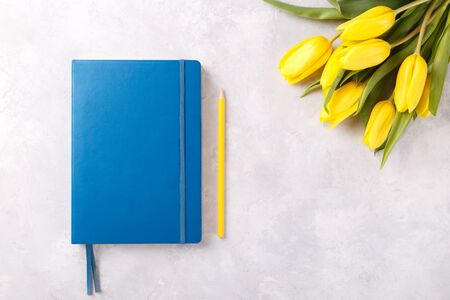 Blue notepad, pencil and bouquet of spring yellow tulips on grey stone table top view ,flat lay