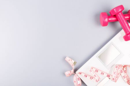Weight loss concept flat lay with scales, dumbbells and measuring tape on grey background, copy...