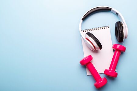 Pink dumbbells, notepad and headphones on blue background, flat lay copy spaceの写真素材