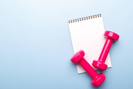 Pink dumbbells and notepad on blue background, flat lay copy spaceの写真素材