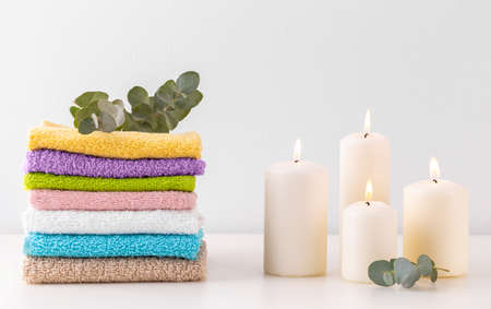 Stack of colorful bath towels, branch of eucalyptus and candles over pastel background