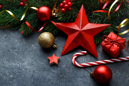 Christmas flat lay with red star, gold ornaments and fir tree branch on black stone background with copy spaceの写真素材