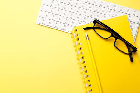 Student or freelancer workspace with keyboard, glasses, notepad, pencil on yellow background, flat...