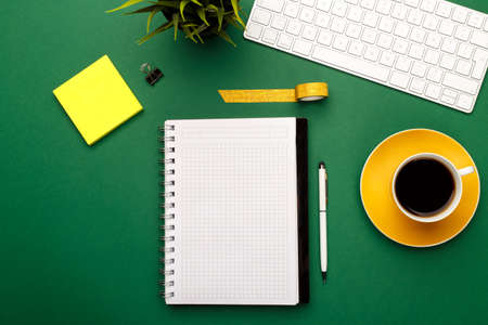 Student, business or freelancer workspace with keyboard, coffee, notepad, pen and pencils on green...