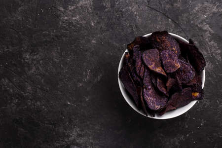 Purple sweet potato chips on black stone background, healthy snack top view with copy spaceの写真素材