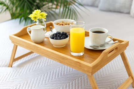 Wooden tray with breakfast on the bed in a hotel room, romantic morning with healthy foodの写真素材