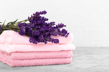 Stack of pink cotton towels and bouquet of lavender flowers on the grey stone trendy background,...