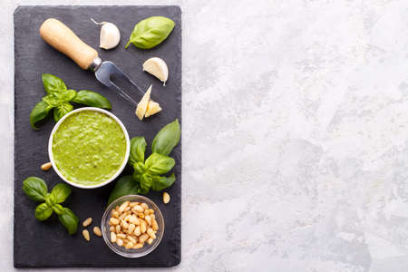 Pesto sauce and ingredients, cheese, basil, garlic, pine nuts, olive oil on black cheese board and grey stone background with copy spaceの写真素材
