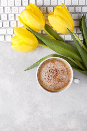 Yellow tulips cup of coffee and keyboard on grey stone table, top view flat layの写真素材