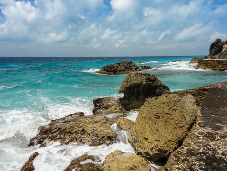 The waves of the blue sea breaking on large reefs on the shore on the background of sky with cloudsの写真素材