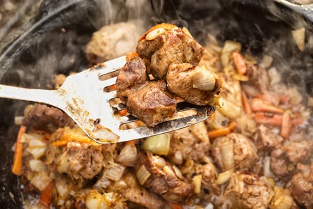 Meat with carrots and onions in a cauldron on fire with a silver spoonの写真素材