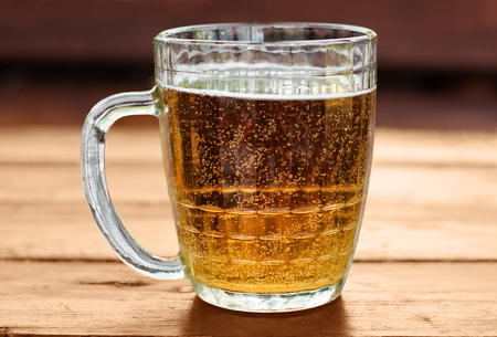 Large mug of beer with foam and bubbles on a wooden table close up