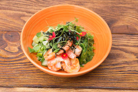Salad with shrimps, seaweed tomatoes and arugula in a plate on a wooden table