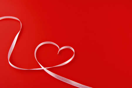 heart made of white ribbon on a red backgroundの写真素材