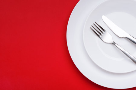 two white plates with a knife and a fork on a red background. minimalistic table settingの写真素材