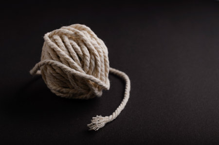 A tightly wound ball of natural rope sits on a dark surface with a loose end gracefully draping to one side, creating a minimalist aesthetic.の写真素材