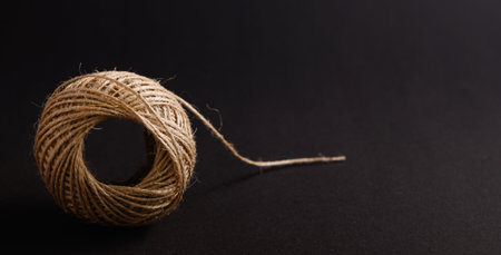A ball of natural twine sits on a black surface, with a thin end trailing off to the side,...