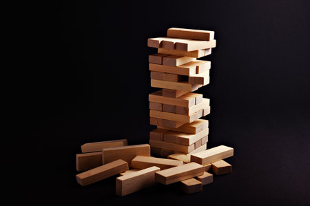 Stacked wooden blocks create a tall structure surrounded by fallen pieces, evoking a sense of...