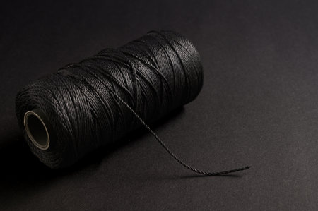 A spool of black thread lies on a dark background, highlighting the intricacies and smoothness of...