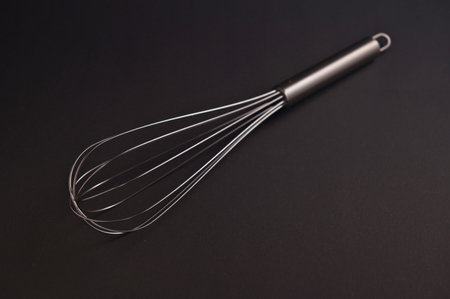 A sleek kitchen whisk lies on a dark surface, waiting to blend ingredients for baking or cooking...