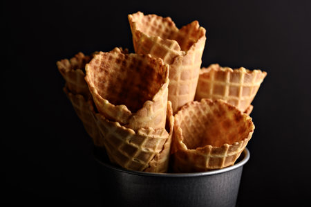 A collection of waffle cones is arranged in a metal container, highlighting the warm tones and intricate patterns of each cone.の写真素材