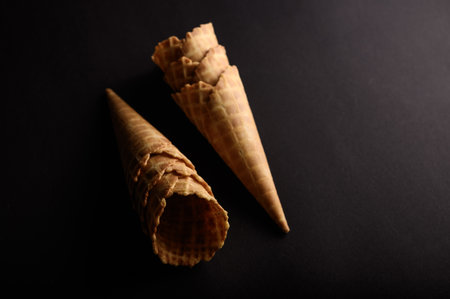 Waffle cones and sugar cones are arranged in a visually appealing manner against a dark backdrop, showing their textures.の写真素材