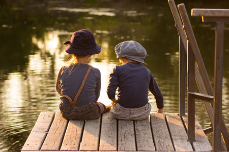 Kids sitting with sticks in hands on the river bankの写真素材