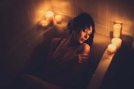 beautiful romantic woman in a bathtub with candles, warm and cozy color toningの写真素材