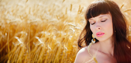 A field of wheat. Beautiful woman eyes closed, sensual lips. Ears of Golden wheat closeup. The concept of a rich harvest. Copy space for your text. A wide banner. Summer saleの写真素材