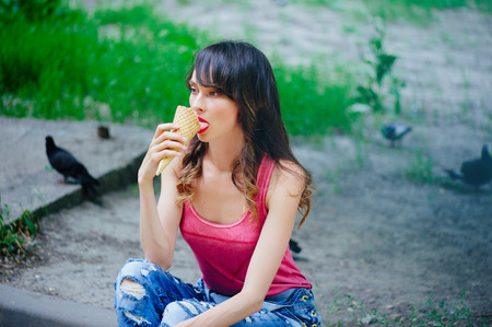 beautiful woman eating ice cream sitting on the sidewalk in the city, summer heatの写真素材