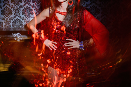 beautiful fashionable woman in red dress waving in the interior, the movement of the dress and light...
