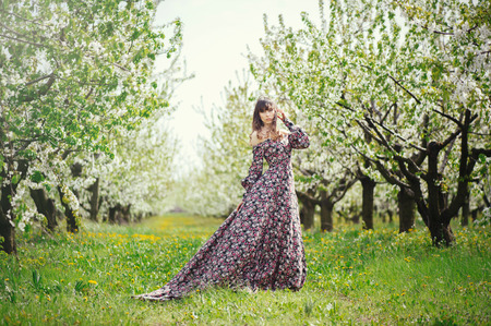 happy beautiful woman in a long dress in a flowered gardenの写真素材