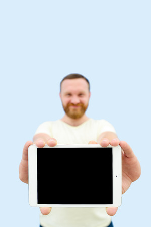 Happy Handsome young man with a beard showing something on a tablet isolated on a blue background, close-up for your text.の写真素材