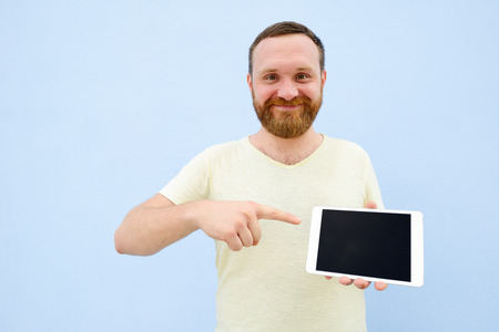 cheerful man with a red beard points at the tablet, space for text.の写真素材
