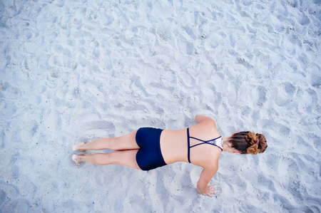 A fit girl trains in the air doing stretching exercises. Beautiful young sporty woman pushing up fitness on sand. Place to paste text. concept of health and energy.の写真素材