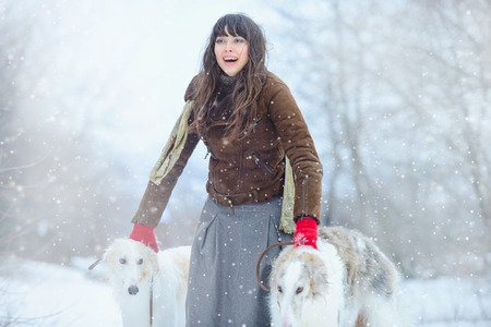 Christmas walk. Beautiful surprised woman in winter clothes with greyhound dogs graceful winter background with snow, emotions. portrait of a woman. New Year.の写真素材
