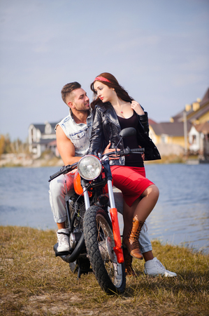 stylish and trendy couple in love on a motorcycle flirting close-up on a background of late autumn in the park,の写真素材