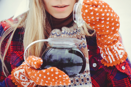 Woman holding a winter brewer of a shaking tea close up on a light background. Woman hands in teal gloves, holding in a cozy transparent with hot tea, cane. The concept of winter and Christmas.の写真素材