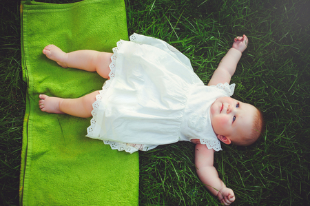 half-year-old child lies on the grass in the yard, dressed in a white dress rejoices, 6 months. Concept education of children, children's goods.の写真素材