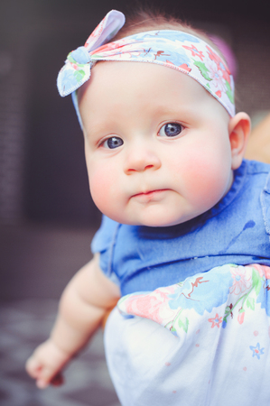 the portrait of a six-month-old child rejoices, is dressed in a blue dress and a headband, 6 months. Concept education of children, children's goods.の写真素材