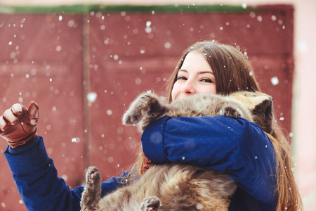 Winter portrait of a young woman with a cat. Beauty Joyous Model A girl laughs and is happy to have a dark red background. Beautiful young woman outdoors. Enjoy nature, in winter.の写真素材