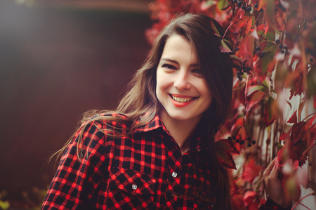 Smiling young brunette woman posing in the courtyard of her residence in a red checkered shirtの写真素材