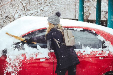 Winter portrait of a young woman cleaning snow from a car. Beauty blonde Model Girl laughs and cheerfully cleans the snow. Beautiful young woman outdoors.の写真素材