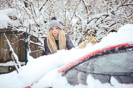 Winter portrait of a young woman cleaning snow from a carの写真素材
