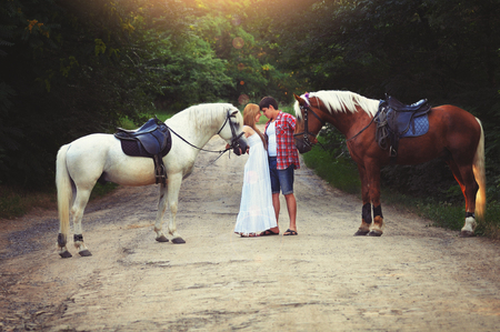 beautiful loving couple with horses stand in the woods on the road, cozy and warm artistic image, flying bright day.の写真素材