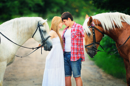 beautiful loving couple with horses stand in the woods on the road, cozy and warm artistic image, flying bright day.の写真素材