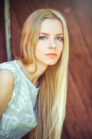 blonde woman on a red wooden background has her hair painted in a pink striped strip, shy and inquisitive.の写真素材