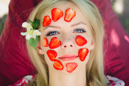 Beautiful woman with a strawberry mask, close-up, facial, natural cosmetics, lying on nature in a summer garden.の写真素材