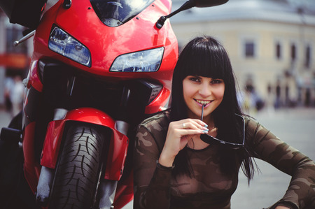 happy woman biker sitting near motorcycle and happy, close-up brunette with red bike.の写真素材